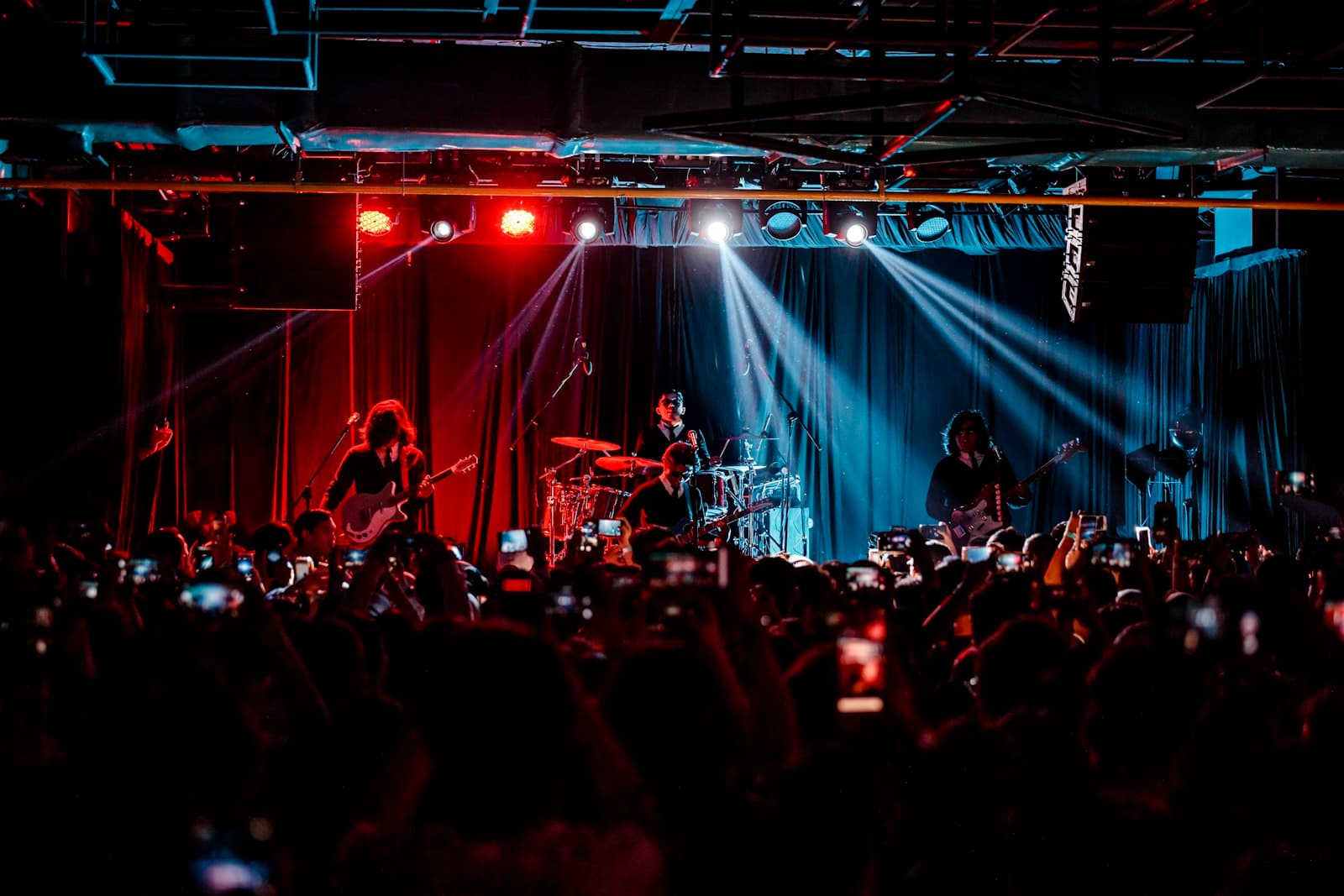 Banda tocando ao vivo em cima de um palco, com plateia ao fundo