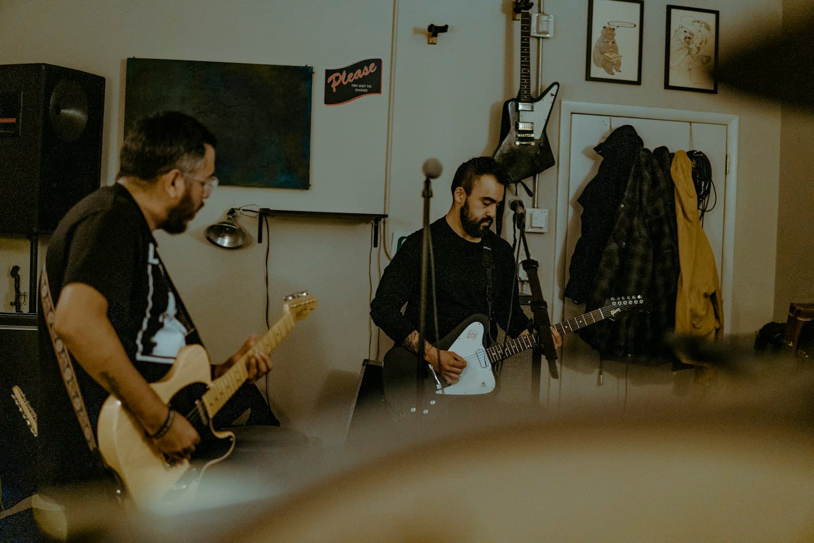 Dois músicos tocando guitarra e violão sentados numa sala de ensaio